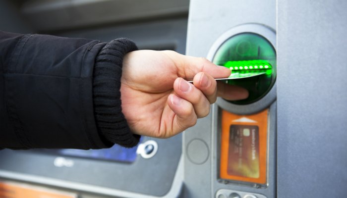 A close up of a person’s hand inserting a card into an ATM.