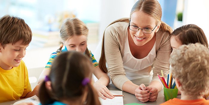 A teacher interacting a group of children as they draw in workbooks.